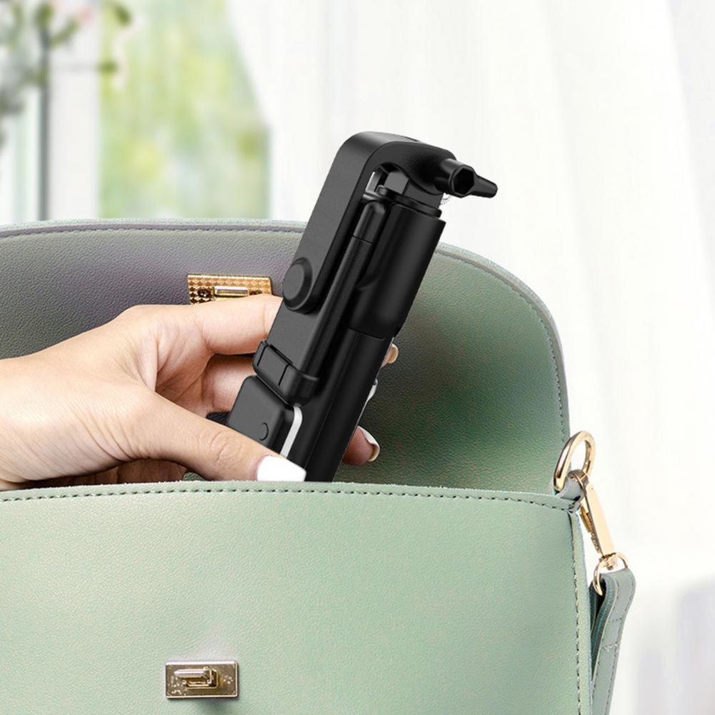 Compact black selfie stick held in hand, partially inside mint green purse with gold accents