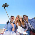 Group taking beach selfie with smartphone selfie stick, travel gear for vacation photos